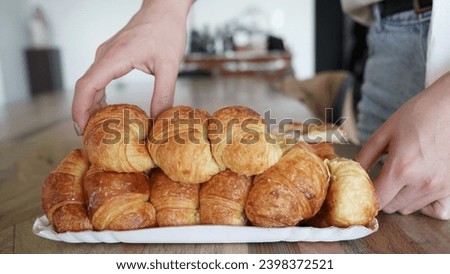 Closeup view of a woman grabbing a butter based croissant from the dozen. 