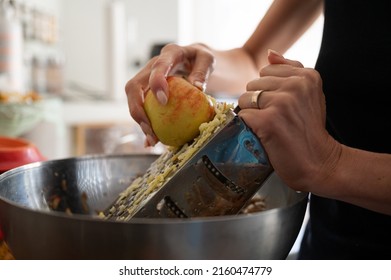 Closeup view of a woman grating an apple for apple strudel filling on a home kitchen counter.