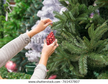 Closeup view of woman hands dressing up a Christmas tree with a red toy.