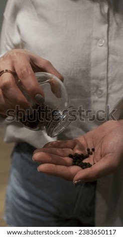 Closeup view of a woman holding a glass jar with black pepper grains