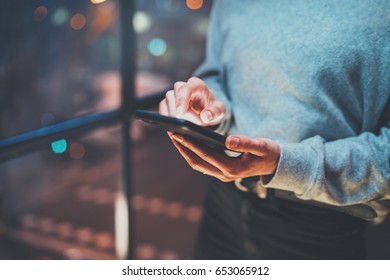 Closeup View Of Woman Holding Modern Mobile Phone In Hands.Girl Pointing Fingers On Empty Touch Mobile Screen At Night. Horizontal, Blurred Background, Bokeh Effects