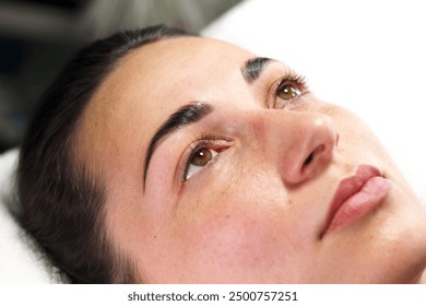 A close-up view of a woman lying down after receiving eyebrow tinting. Her eyes are open, highlighting the fresh tint on her eyebrows and the natural look of her facial features. - Powered by Shutterstock