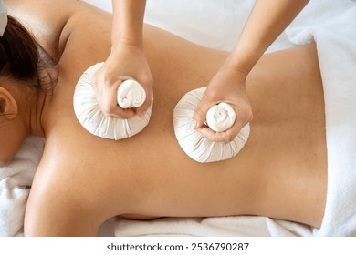 Close-up view of a woman receiving two herbal compress massage on her back, focusing on therapeutic relaxation and wellness in spa - Powered by Shutterstock