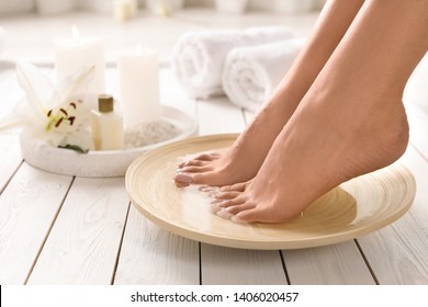 Closeup view of woman soaking her feet in dish with water on wooden floor, space for text. Spa treatment