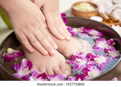 Closeup View Of Woman Soaking Her Hand And Feet In Dish With Water And Flowers On Wooden Floor. Spa Treatment And Product For Female Feet And Hand Spa. Orchid Flowers In Ceramic Bowl.