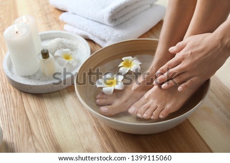Closeup view of woman soaking her feet in dish with water and flowers on wooden floor. Spa treatment