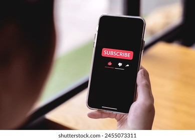 Close-up view of a woman using a smartphone to press red subscribe button on online media. Concepts of technology and following news, hot trends and new content on social media - Powered by Shutterstock