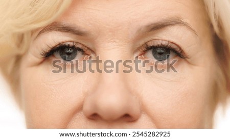 Close-up view of woman's eye, emphasizing wrinkles and calm, serene gaze against white studio background. Lashes and brows. Concept of natural beauty, spa treatment, cosmetology.