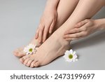 Closeup view of woman`s groomed feet after care procedure and beautiful flowers on grey background