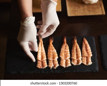 Closeup view of woman's hands in gloves are preparing shrimp for rolling sushi in restaurant - Powered by Shutterstock