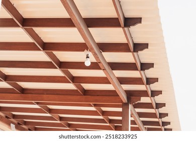 A close-up view of a wooden ceiling structure with exposed beams and a single light bulb hanging from it. The ceiling features a combination of wooden and metal elements, creating a modern aesthetic. - Powered by Shutterstock