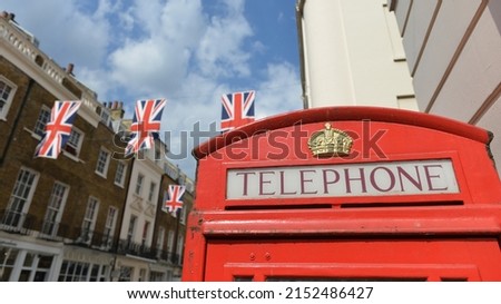 Close-up view of the word 'Telephone' on a traditional red British phone box on a London street with buildings and UK union flags in the background 
