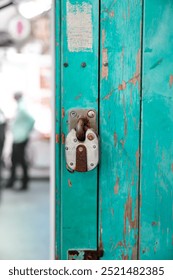 A close-up view of a worn, rusted padlock on a turquiose or teal blue green painted door showing signs of wear and tear. The lock is old and worn, with visible rust.  paint peeling off the wooden door