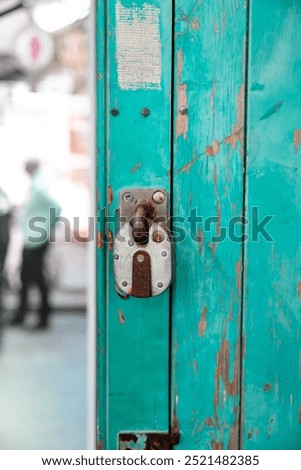 A close-up view of a worn, rusted padlock on a turquiose or teal blue green painted door showing signs of wear and tear. The lock is old and worn, with visible rust.  paint peeling off the wooden door