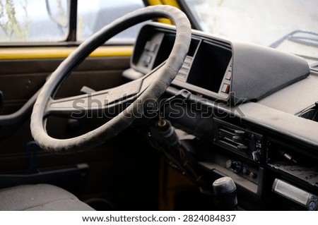 Close-up view of the worn steering wheel and dashboard inside an abandoned vintage van. Aged interior with weathered materials creates a nostalgic atmosphere suitable for transportation, automotive, decay, restoration and abandoned vehicle concepts.