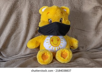 Close-up view of a yellow and white coloured teddy bear laying on a sofa using a black face mask during the Covid-19 pandemia. - Powered by Shutterstock