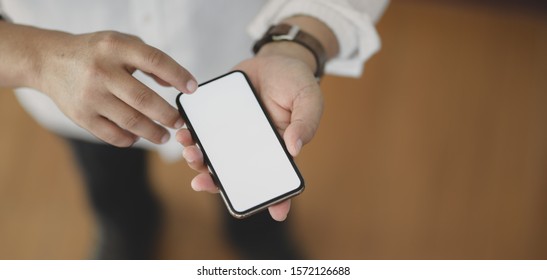 Close-up view of young man using blank screen smartphone while standing in his office room 
