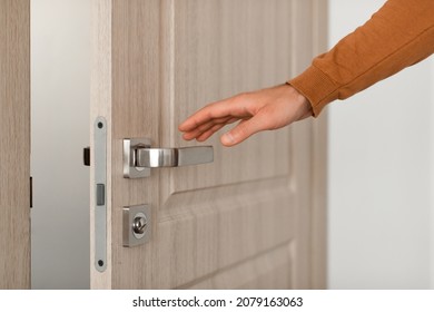 Closeup view of young unrecognizable man opening wooden door, reaching hand to handle doorknob, male visitor standing in entrance or exit, guest person wants to come in or leave, selective focus