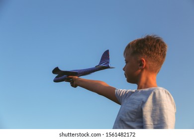 Closeup View Of Young White Kid Holding Toy Plastic Blue Plane In Hand. Confident Boy Setting Big Goals Concept. Horizontal Color Photography.