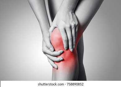 Closeup view of a young woman with knee pain on gray background. Black and white photo with red dot.