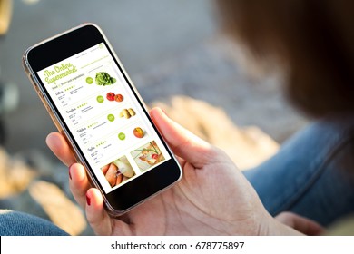 close-up view of young woman shopping groceries on online supermarket with her mobile phone. All screen graphics are made up.