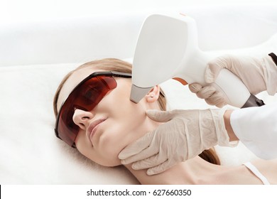 Close-up view of young woman in uv protective glasses receiving laser skin care on face - Shutterstock ID 627660350