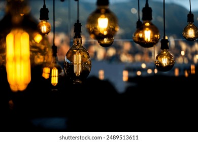 Close-up of vintage Edison bulbs glowing warmly against a blurred cityscape. Ideal for illustrating ambiance, interior design, and urban nightlife. Perfect for blogs, advertisements, or design project - Powered by Shutterstock