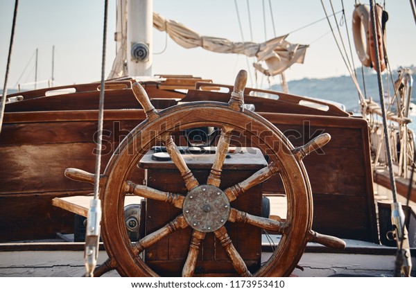 Closeup of a vintage hand wheel on a\
wooden sailing yacht. Yachting, helm of old wooden sailboat in port\
of sailing, rope, steering wheel, details of\
yacht.