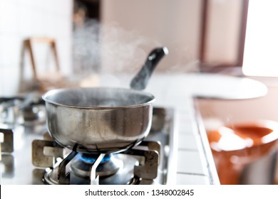 Closeup Of Vintage Tiled Gas Stove Top With Tiles White Countertop And Stainless Steel Pot And Steam Cooking With Blue Flame In Retro Kitchen