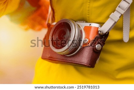 Close-up of a vintage-style camera in a leather case, worn over the shoulder of a person dressed in a yellow jacket. The warm sunlight creates a nostalgic and inviting atmosphere, perfect for promotin