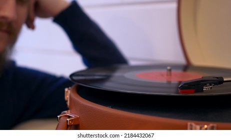 A Close-up Of A Vinyl Record Is Spinning In The Player, In The Background An Unrecognizable Person Is Listening To Music. Vintage Music, Early 20th Century Use Of The Gramophone To Listen To Music.