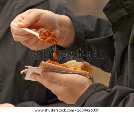 Close-up of a visitor eating pulled meat with vegetables on flatbread using a wooden fork at a food festival in Karlin, Prague, lively street food atmosphere.