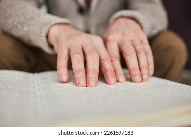 Close-up of visually impaired senior man using his hands to read book in Braille at table - Powered by Shutterstock