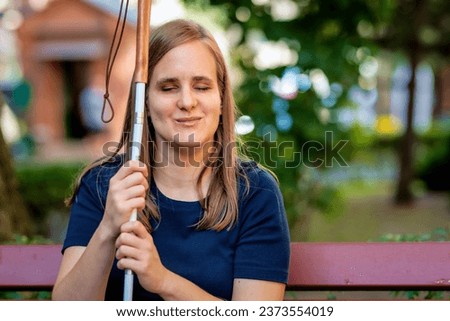 Close-up of a visually impaired woman holding a white cane and sitting on a bench in the city. Smiling female wearing casual clothes.  Stock foto © 