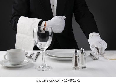 Closeup Of A Waiter In A Tuxedo Setting A Formal Dinner Table. Shallow Depth Of Field In Horizontal Format On A Light To Dark Gray Background. Man Is Unrecognizable.