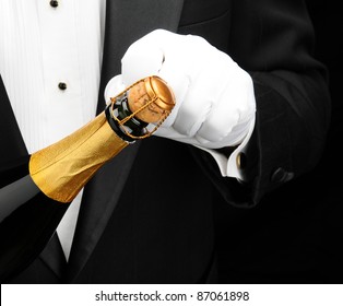 Closeup of a waiter wearing a tuxedo opening a bottle of champagne. Hand bottle and torso only. Man is unrecognizable.