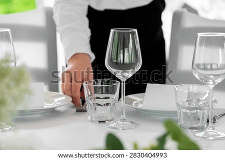 Close-up of a waiter's hand setting a table with plates, wine glasses, and water tumblers at a formal event or restaurant