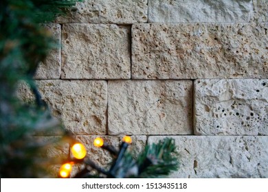 Closeup Of The Wall Of Beige Cream Brick With Blurred Yellow Lights And Fir Bough. Brick Texture With Small Items. Building Textured Background. Soft Selective Focus.