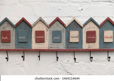 Closeup Wall Hanger. Funny Hanger In The Form Of Houses With The Signatures Of The Days Of The Week In French. Vintage Coat Hanger Hanging On A White Brick Wall.