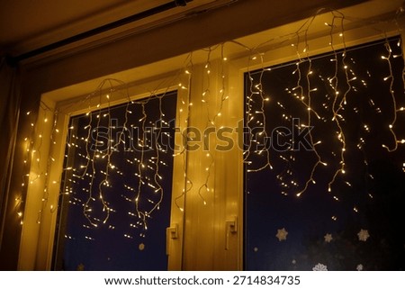 Close-up of warm yellow string lights hanging indoors on a window, creating a festive curtain effect against the dark night.