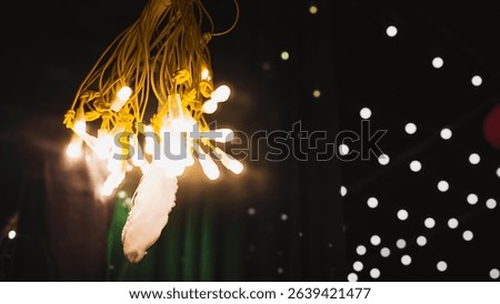 Closeup of warmtoned string lights with yellow wires, hanging, softly illuminating a dark background. Bokeh effect of more lights in distance.