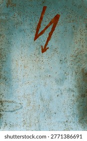 Close-up of warning mark on rusty metal electrical cabinet door, showing aged utility equipment surface in a rustic interior.