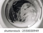  Close-up of a washing machine in action, with foam and bubbles during the wash cycle. Clean clothes, modern appliance, and everyday home life concept.