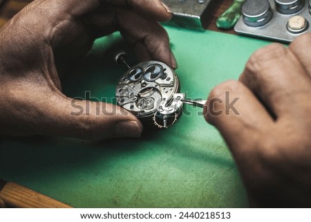 Close-up of a watchmaker's hands removing a part of a watch with great precision using tweezers. The small, precise gears of the device can be seen.
