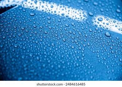 Close-up of water droplets demonstrating the hydrophobic effect on a car surface after applying a ceramic coating. The image shows a glossy, well-protected blue car surface in a detailing studio