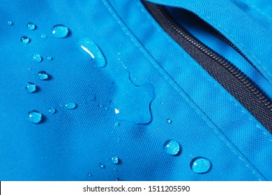 Closeup of water drops on bright blue fabric and black zipper with waterproof design to protect fabric of the cloth from humidity and to offer easy cleaning to users Fabric texture with design concept