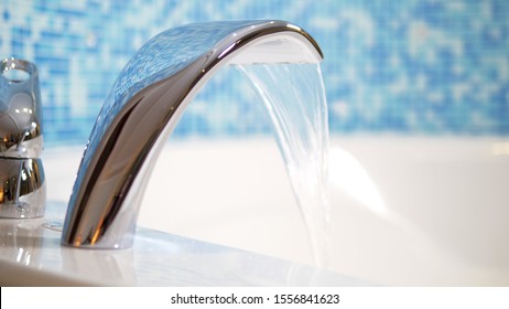 close-up. water flows from a luxurious water tap into a large modern bathtub against a blue mosaic wall - Powered by Shutterstock