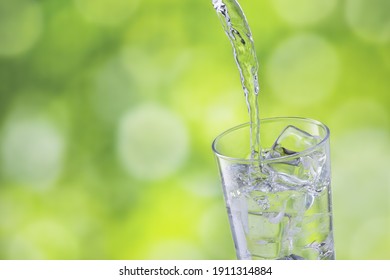 closeup water pouring into glass with ice on green blurred background