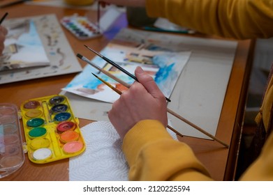 Closeup Of Watercolor Painting Process. Brush In Hand Above Painting. Colorful Medieval City Street On Paper Board.