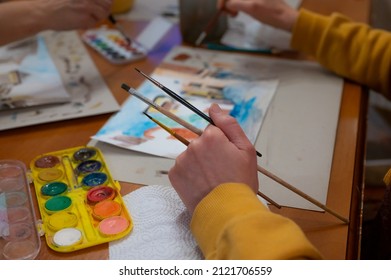 Closeup Of Watercolor Painting Process. Brush In Hand Above Painting. Colorful Medieval City Street On Paper Board.